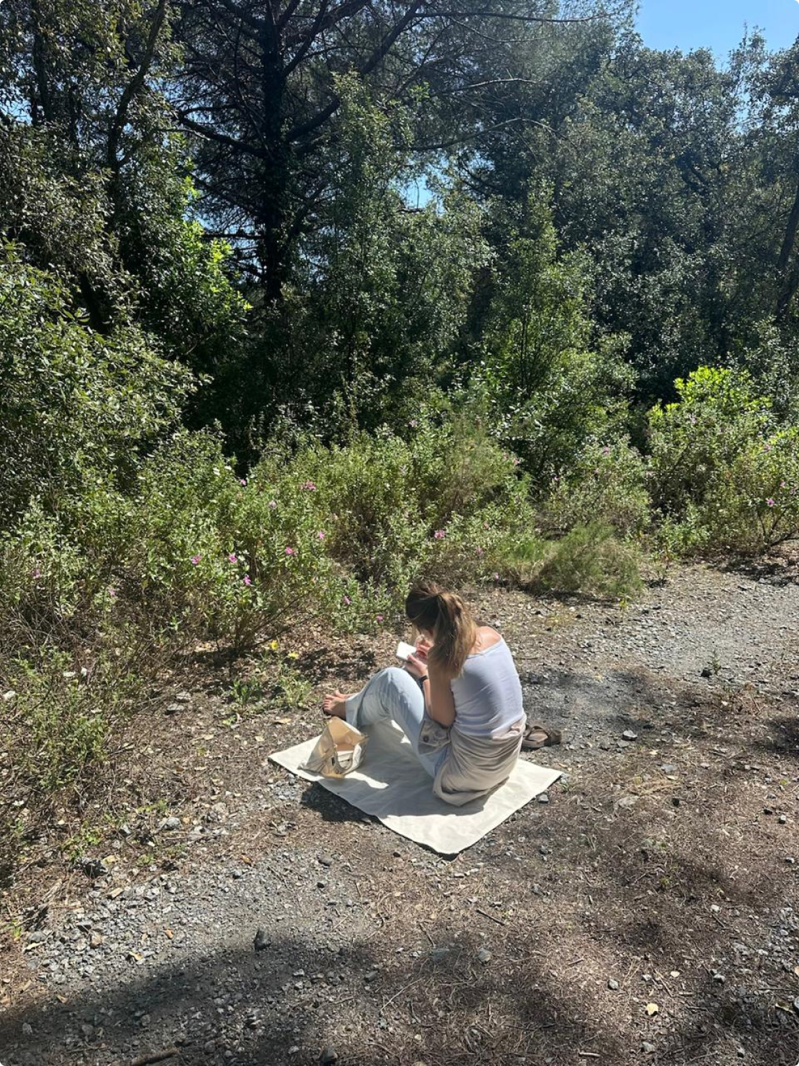 Caro painting outdoors among trees, sitting on a blanket